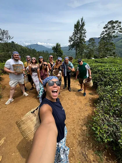 Un groupe WeRoad pose pour un selfie sur un sentier dans une plantation de thé, tenant des paniers tressés pour la cueillette du thé.