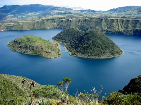 Una vista dall'alto di due isole verdi in un lago craterico blu intenso, circondato da dolci colline sotto un cielo sereno.