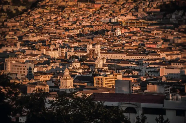 Un vasto paesaggio urbano di edifici storici e tetti in tegole che si estende su una collina al tramonto.