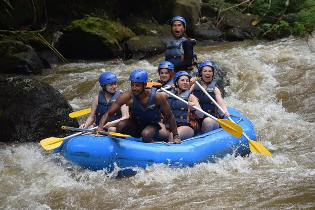 Eine WeRoad-Gruppe paddelt, mit Helmen und Schwimmwesten ausgestattet, in einem blauen Schlauchboot durch wilde Fluss-Stromschnellen.