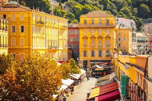 A high-angle view of a bustling street lined with yellow buildings, market stalls, and trees with autumn foliage.