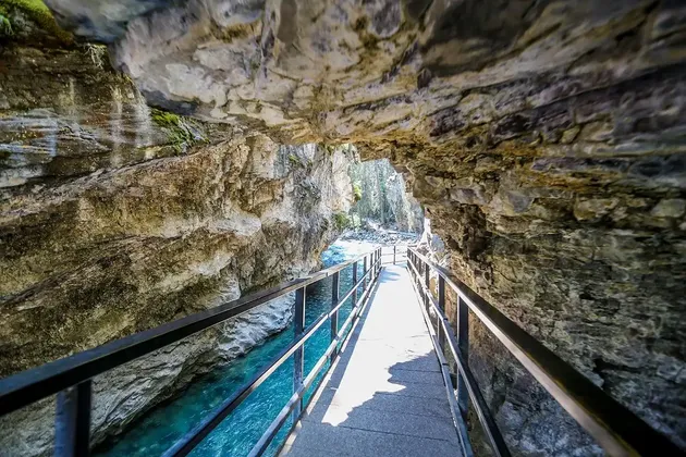 Una passerella sospesa con ringhiera metallica attraversa uno stretto canyon roccioso lungo un fiume turchese.