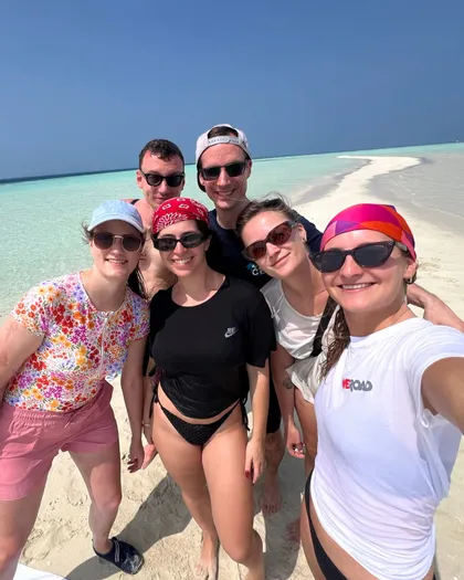 Eine WeRoad Gruppenreise von sechs Personen, die für ein Selfie auf einer weißen Sandbank neben türkisblauem Wasser unter einem klaren blauen Himmel lächeln.