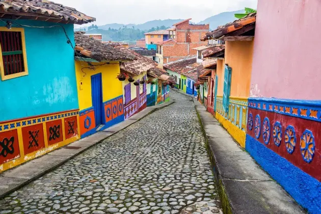 Una strada acciottolata sale in salita, fiancheggiata da edifici dipinti con colori vivaci come turchese, giallo e rosa.