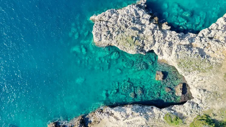 Una vista aerea dall'alto di una costa rocciosa aspra e chiara che incontra un mare limpido e turchese.