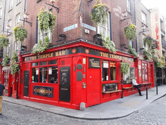 La facciata rosso brillante del pub The Temple Bar su un angolo di strada acciottolata, ornata da cesti di fiori appesi.