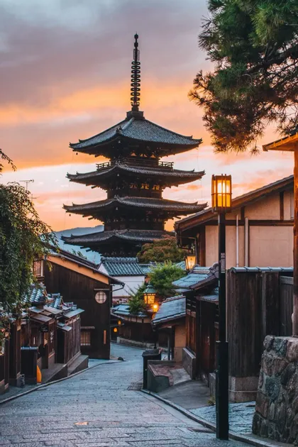Una pagoda a più livelli si erge alla fine di una tradizionale strada in pietra con case di legno contro un cielo al tramonto.
