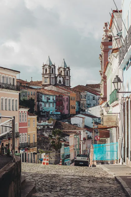 Una vista lungo una ripida strada acciottolata fiancheggiata da colorati edifici storici, con una chiesa a doppia torre visibile in lontananza.