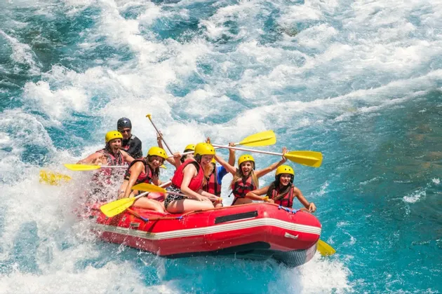 Eine WeRoad-Gruppe jubelt beim Wildwasser-Rafting in einem roten Schlauchboot auf unruhigem blauen Wasser.