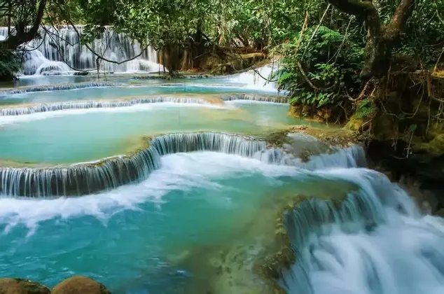 Foto a lunga esposizione di cascate a gradoni con acqua turchese in una giungla lussureggiante.