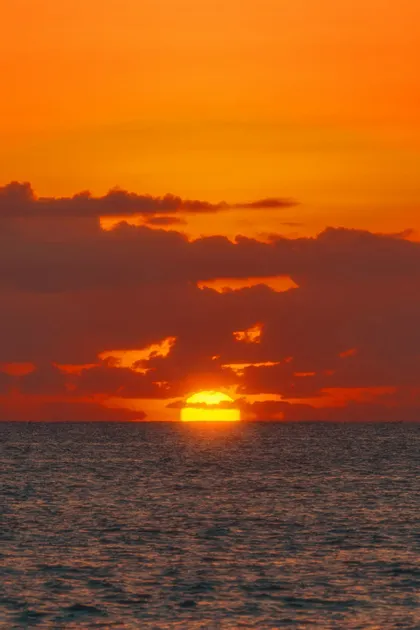 Le soleil jaune se couche sur l'horizon de l'océan sous un ciel orange vif rempli de nuages sombres.