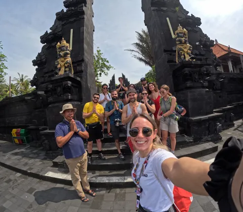 Un viaje en grupo de WeRoad posa para una selfie con un guía, haciendo un gesto de oración frente a una tradicional puerta de piedra negra.