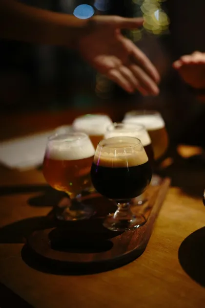 Primo piano di un flight di degustazione di birra artigianale con cinque birre diverse in bicchieri su una paletta di legno.