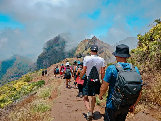 Un gruppo WeRoad in escursione lungo un sentiero di pietra su una cresta di montagna sotto un cielo parzialmente nuvoloso.