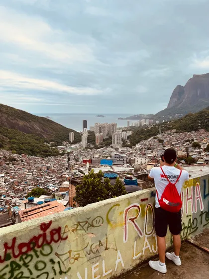 Un leader WeRoad fotografa la vista di una favela e dello skyline cittadino che digrada verso il mare, da un muro ricoperto di graffiti.