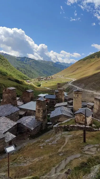 Un borgo di case in pietra e torri adagiato in una verde valle montana sotto un cielo parzialmente nuvoloso.