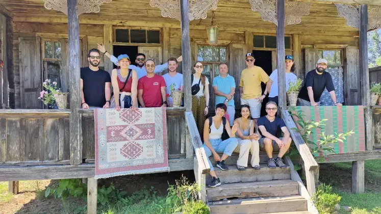 Un gruppo WeRoad in posa per una foto sul portico e sui gradini di una casa rustica in legno, con in mano un tappeto a motivi.