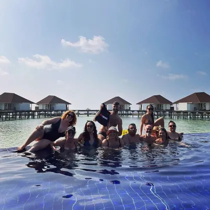 Un gruppo WeRoad in viaggio posa in una piscina a sfioro, con bungalow sull'acqua visibili sullo sfondo sotto un cielo azzurro.