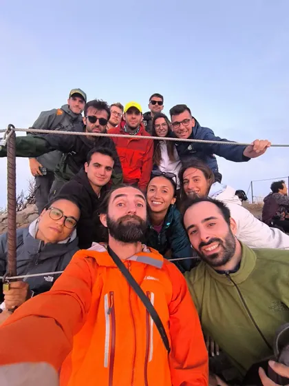 Un viaggio di gruppo WeRoad con persone sorridenti, in giacche da esterno, che posano per un selfie di gruppo su una collina.