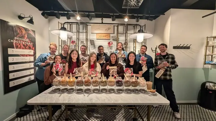 Un gruppo WeRoad in viaggio posa per una foto in un laboratorio di cioccolato, mostrando i cioccolatini appena fatti.