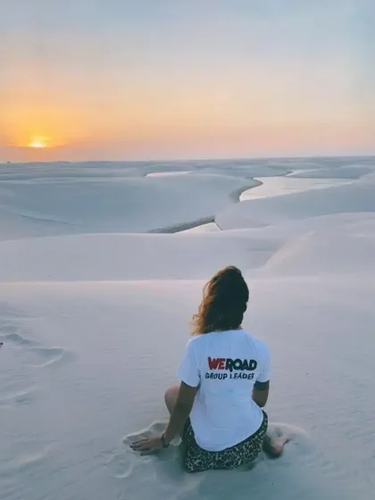 Un capogruppo WeRoad siede su una duna di sabbia bianca, guardando il tramonto su un paesaggio di lagune serpeggianti.