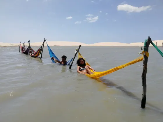 Un viaggio di gruppo WeRoad si rilassa in amache colorate sospese su una laguna, con dune di sabbia sullo sfondo.