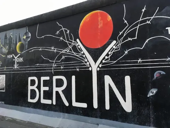 Un murale dipinto su un muro di cemento con la parola BERLINO in grandi lettere bianche sotto un sole rosso e grafiche di filo spinato.