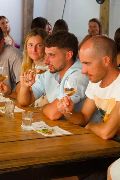 Un viaggio di gruppo WeRoad con persone sedute a un lungo tavolo di legno per una degustazione di vino rosé.