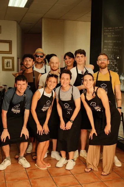 Un gruppo WeRoad in posa per una foto con grembiuli neri abbinati durante una lezione di cucina.