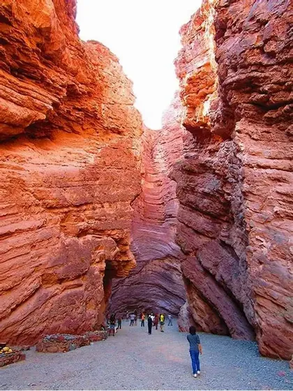 Un viaggio di gruppo WeRoad attraversa uno stretto passaggio in un canyon con alte pareti di roccia rossa stratificata.