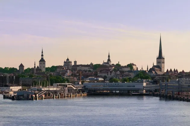 Skyline storico della città con guglie e torri di chiese in evidenza, visto dall'acqua, con un moderno porto in primo piano.