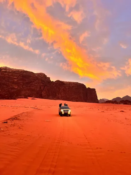 Eine WeRoad Gruppenreise im Geländewagen über rote Wüstensanddünen unter einem Sonnenuntergangshimmel.
