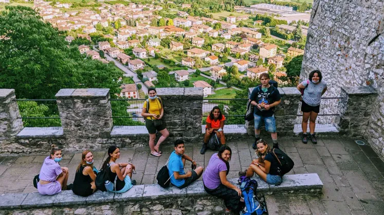 Un grupo de WeRoad posando en un mirador de piedra con vistas a un pueblo de casas con tejados rojos en un valle verde.