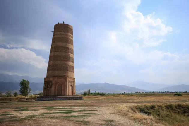 Un alto minareto in mattoni si erge in un vasto paesaggio arido, con due persone in cima e montagne all'orizzonte.