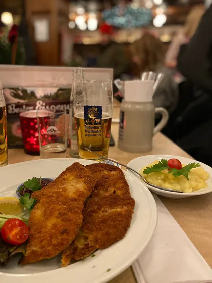 Una cotoletta impanata con insalata di patate e un bicchiere di birra Augustiner su un tavolo da ristorante.