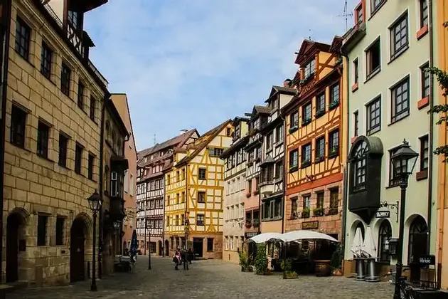 Una strada acciottolata curva tra file di colorati e storici edifici a graticcio sotto un cielo parzialmente nuvoloso.