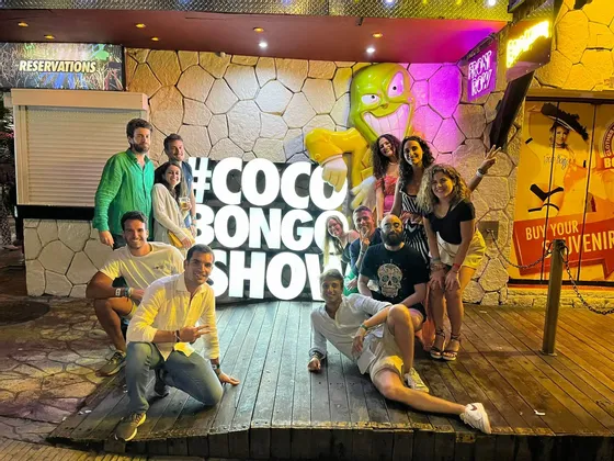 Un grupo de WeRoad posa para una foto de noche delante de un gran cartel luminoso que dice '#COCO BONGO SHOW'.