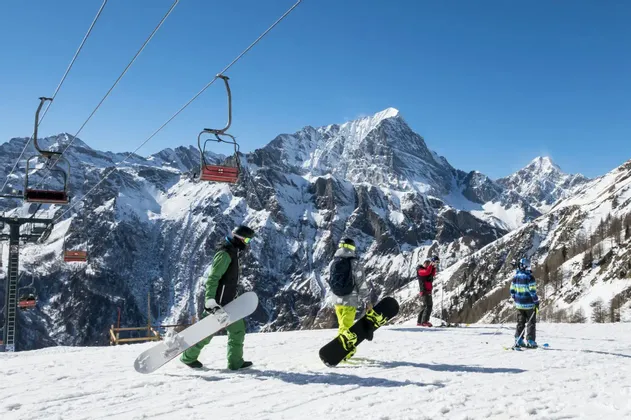 Eine WeRoad-Gruppenreise mit Snowboardern auf einem verschneiten Hang, mit einem Sessellift und Bergen im Hintergrund.