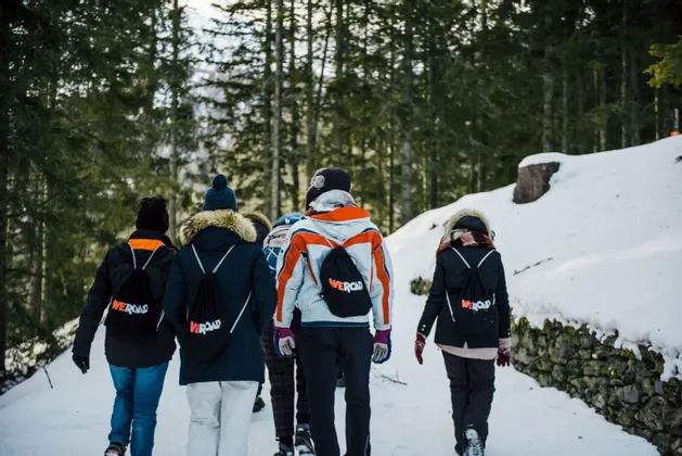 Eine WeRoad-Gruppe wandert auf einem verschneiten Pfad durch einen Kiefernwald, von hinten gesehen.