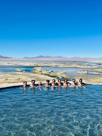 Un viaggio di gruppo WeRoad in posa per una foto mentre si rilassa in una sorgente termale naturale, con un vasto paesaggio arido sullo sfondo.