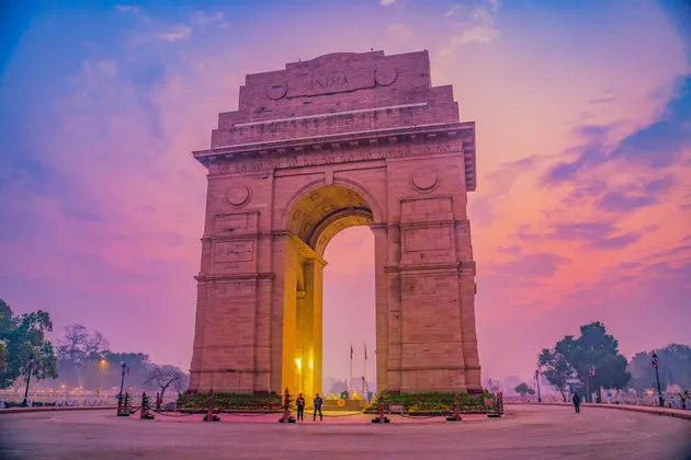 L'India Gate, un imponente arco in pietra, è illuminato contro un cielo rosa e viola dai colori vivaci all'alba.