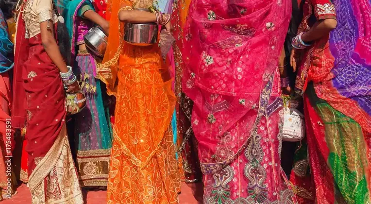 Eine Gruppe von Frauen steht eng beieinander, trägt leuchtende und farbenfrohe traditionelle indische Saris und hält kleine Töpfe.