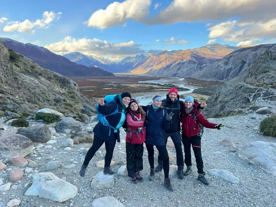 Eine WeRoad-Gruppe von fünf Personen in Wanderausrüstung posiert auf einem felsigen Wanderweg vor einem Bergtal.