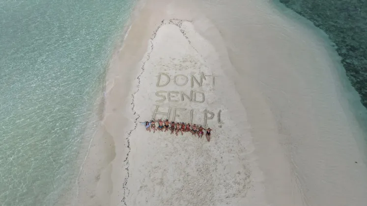 Eine WeRoad Gruppenreise auf einer Sandbank, neben den Worten "DON'T SEND HELP!" im Sand, umgeben von klarem Wasser.