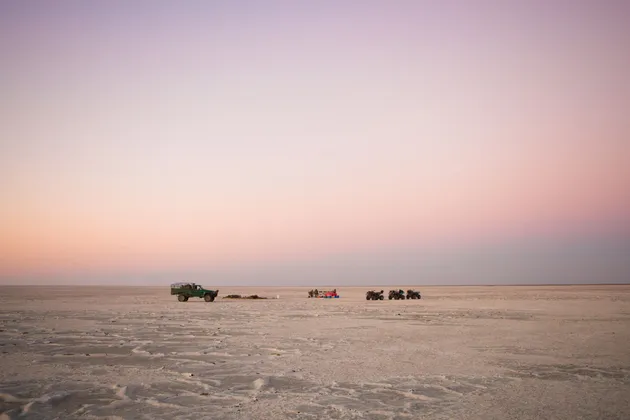 Un viaggio di gruppo WeRoad in pausa su una distesa di sale desertica con quad e un fuoristrada al tramonto