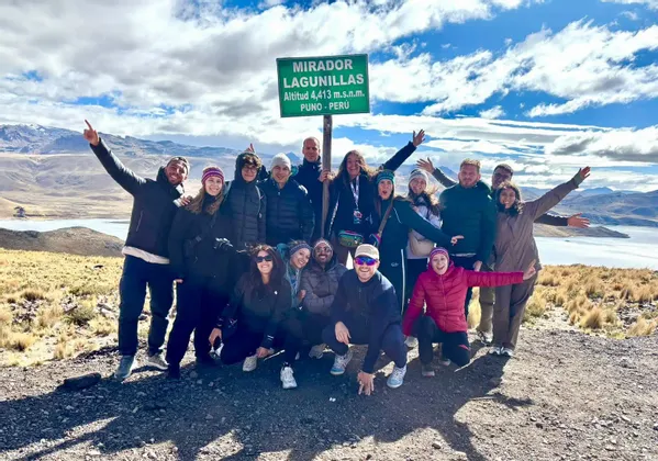 Un viaggio di gruppo WeRoad in posa all'aperto accanto a un cartello alpino verde con montagne e un lago alle loro spalle