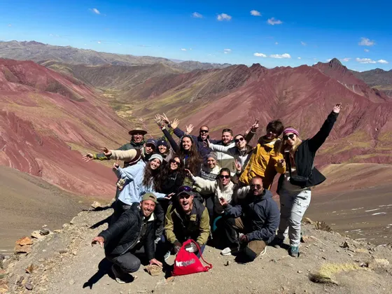 Un viaggio di gruppo WeRoad in posa allegra su una cima di montagna con valli rossastre sullo sfondo