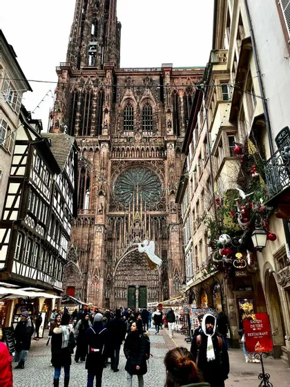 Persone che camminano lungo una strada addobbata fiancheggiata da negozi ed edifici storici verso una imponente cattedrale gotica.