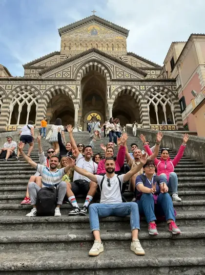 Un viaje en grupo de WeRoad sentado en escalones de piedra y saludando frente a una gran catedral