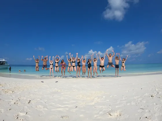 Eine WeRoad-Gruppe, die gemeinsam an einem weißen Sandstrand vor türkisblauem Meer in die Luft springt.